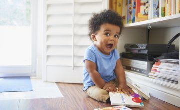 Surprised Black baby boy sitting on floor playing with books